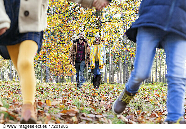 Kinder spielen beim Laufen mit Eltern  die im Hintergrund im Wald laufen