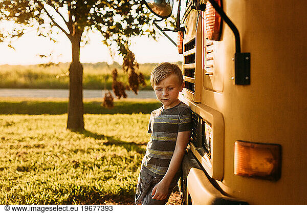 Kindergarten aged child leaning against school bus for back to s