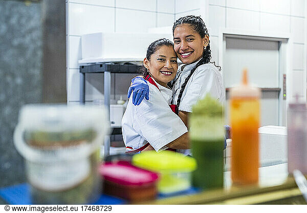 Kitchen assistants in chef's white embracing each other in restaurant