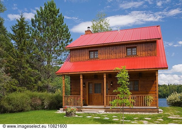 Kleine Blockhausfassade im Landhausstil mit rotem Blechdach und brauner Verkleidung im Sommer