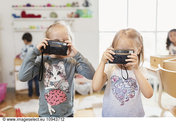 Kleine Mädchen mit Spielzeugkameras im Klassenzimmer