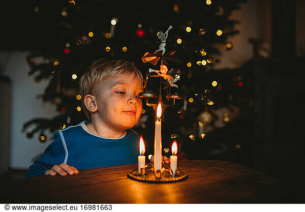 Kleiner Junge bläst Kerzen aus einer Weihnachtskugel mit Baum dahinter aus