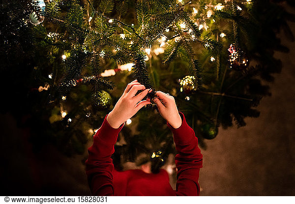 kleiner Junge legt Ornamente auf einen Weihnachtsbaum