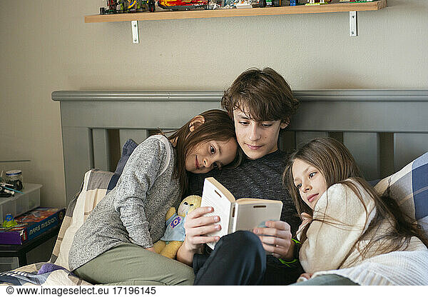 Kleiner Junge liest seinen kleinen Schwestern im Schlafzimmer vor.