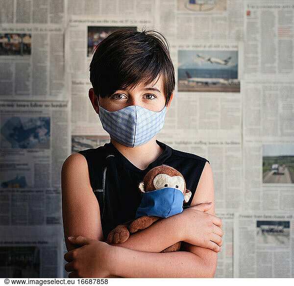 Kleiner Junge mit Maske  der einen Spielzeugaffen vor einem Zeitungshintergrund hält.