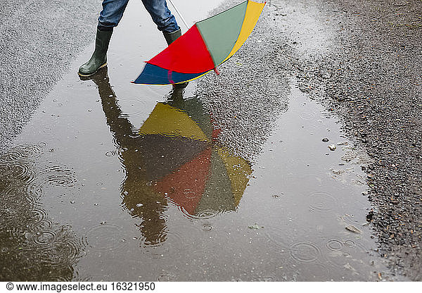 Kleiner Junge mit Regenschirm und Gummistiefeln steht in einer Pfütze  Teilansicht