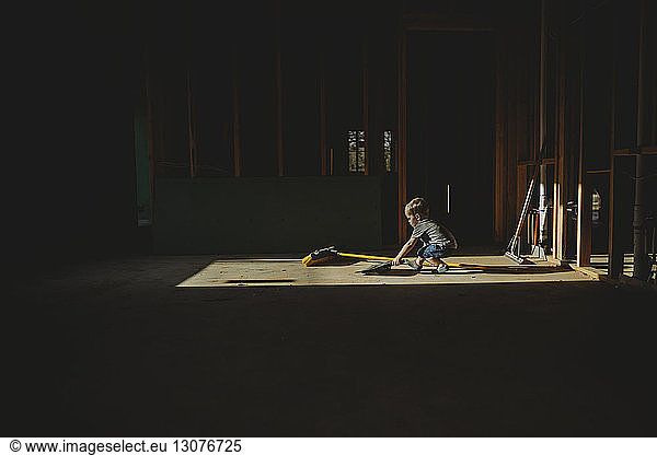 Kleiner Junge mit Reinigungsgerät steht in verlassener Dunkelkammer