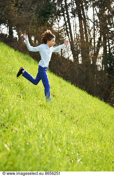 Kleiner Junge rennt steiles Grasfeld hinunter