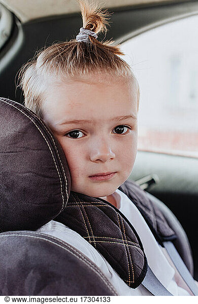 Kleiner Junge von 5 Jahren in einem Kindersitz  der geduldig auf dem Rücksitz eines Autos sitzt