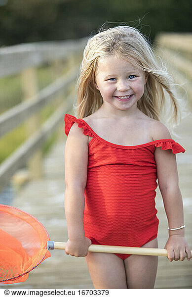 Kleines Mädchen in rotem Badeanzug auf Brücke mit rotem Fischernetz