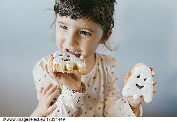 Kleines Mädchen isst selbstgebackene Halloween-Geisterkekse