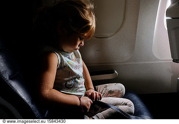 Kleines Mädchen schnallt sich in dramatischem Licht im Flugzeug an