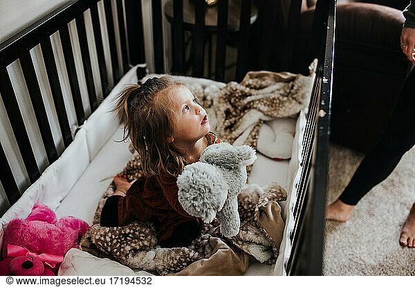 Kleines Mädchen wach in Krippe umgeben von ausgestopften Tieren im Kinderzimmer