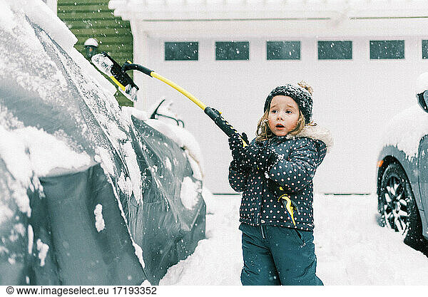 Kleines süßes Kleinkind Mädchen im Schnee Anzug Clearing Autos von Schnee mit Pinsel