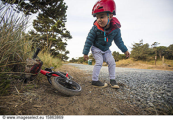 Kleinkind beugt sich vor  um das Fahrrad aufzuheben.