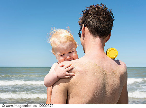 Kleinkind findet Trost bei Vater am Strand