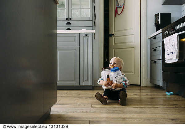 Kleinkind hält Plastikgläser  während es zu Hause in der Küche auf dem Boden sitzt