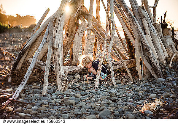 Kleinkind spielt in Treibholzstruktur in der Dämmerung