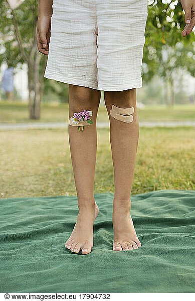 Knees of girl taped with bandage and flowers standing on blanket