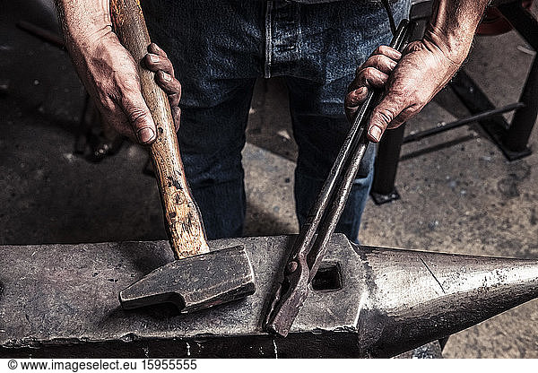 Knife maker holding pliers and hammer on anvil