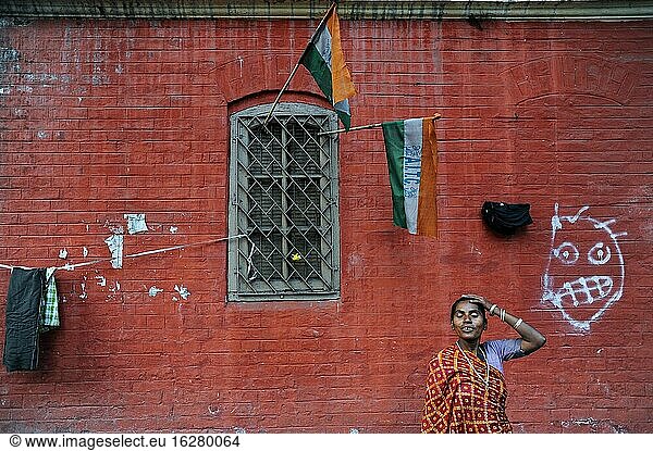 Kolkata (Kalkutta)  Westbengalen  Indien  Asien - Eine Frau in traditioneller Kleidung steht vor einem roten Backsteingebäude am Straßenrand in der New Market Area mit indischen Flaggen und einem Graffiti im Hintergrund.