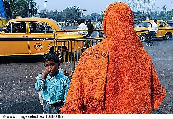 Kolkata (Kalkutta)  Westbengalen  Indien  Asien - Eine Person  die einen orangefarbenen Schal trägt  und ein Kind stehen vor gelben Ambassador-Taxis im Stadtzentrum. Der Ambassador war das erste Auto  das in Indien hergestellt wurde  und wurde von 1958 bis 2014 produziert.