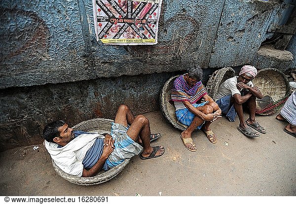 Kolkata (Kalkutta)  Westbengalen  Indien  Asien - Eine Straßenszene in der ostindischen Metropole zeigt Tagelöhner  die sich am Straßenrand ausruhen und darauf warten  mit traditionellen Körben Waren für Kunden zu tragen.