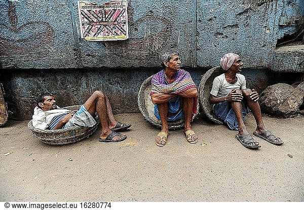 Kolkata (Kalkutta)  Westbengalen  Indien  Asien - Eine Straßenszene in der ostindischen Metropole zeigt Tagelöhner  die sich am Straßenrand ausruhen und darauf warten  mit traditionellen Körben Waren für Kunden zu tragen.