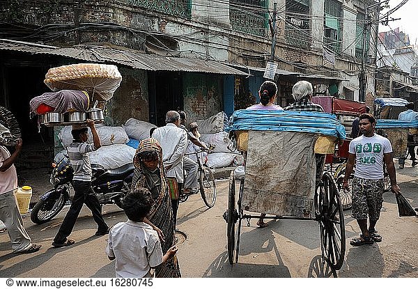 Kolkata (Kalkutta)  Westbengalen  Indien  Asien - Eine Straßenszene zeigt das geschäftige Treiben mit Fußgängern und einer handgezogenen Rikscha auf einer belebten Straße in der ostindischen Metropole. Kalkutta ist die einzige Stadt in Indien  in der noch traditionelle handgezogene Rikschas fahren.