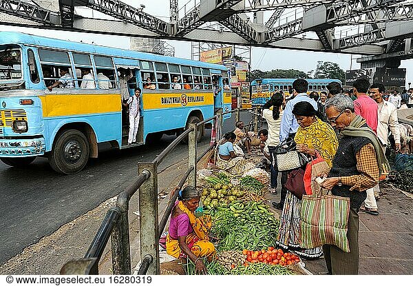 Kolkata (Kalkutta)  Westbengalen  Indien  Asien - Menschen gehen an einem Straßenmarkt an einem Ende der Howrah-Brücke vorbei  während daneben der tägliche Verkehr vorbeifließt.