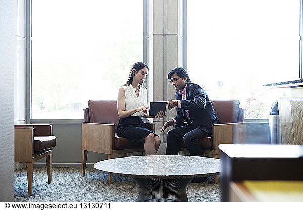 Kollegen diskutieren  während sie einen Tablet-Computer im Büro benutzen