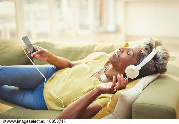 Komfortable reife Frau mit Kopfhörer und mp3-Player auf dem Wohnzimmersofa
