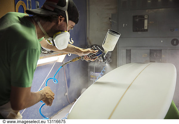 Konzentrierter Arbeiter sprüht weiße Farbe auf Surfbrett
