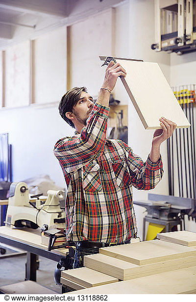 Konzentrierter Mann misst Holzbohlen in der Werkstatt
