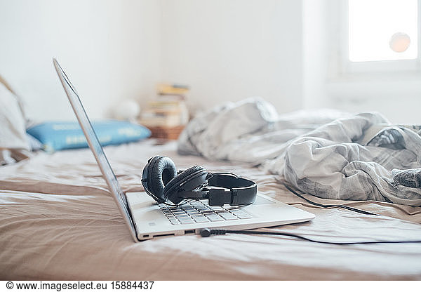 Kopfhörer und Laptop-Computer lagen während der Corona-Virus-Krise auf einem ungemachten Bett.
