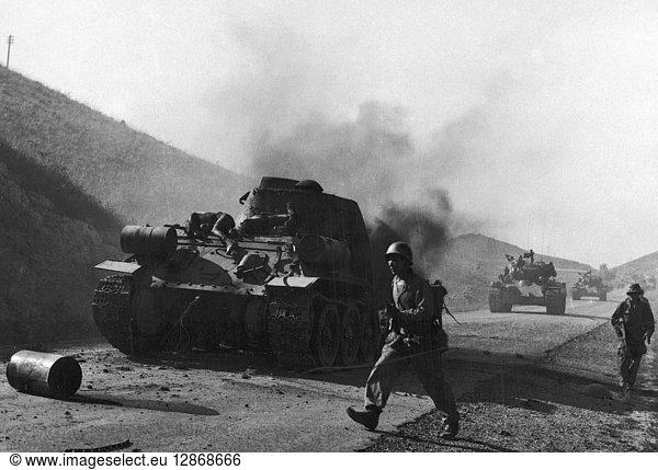 KOREAN WAR: TANKS  1950. U.S. Marine infantrymen followed by tanks pass a burning Communist tank on a Korean highway  September 1950.