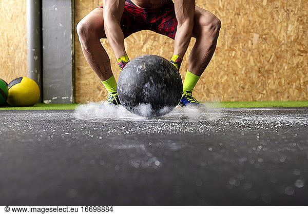 Kräftiger Mann ohne Hemd  der einen schweren Ball gegen den Boden wirft  während er im Fitnessstudio trainiert