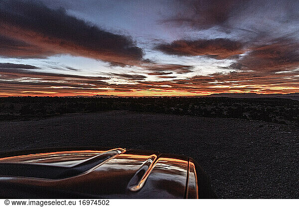 Kräftiger Sonnenaufgang in der Wüste spiegelt sich auf der Motorhaube eines geparkten Fahrzeugs