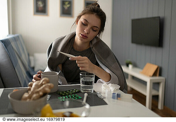 Kranke Frau mit Tee zur Kontrolle des Thermometers