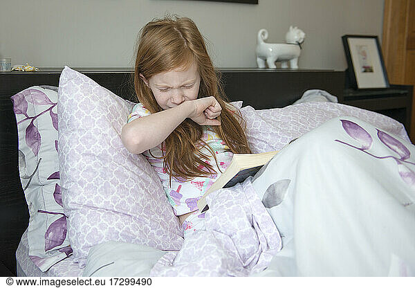 Krankes kleines Mädchen liest im Bett