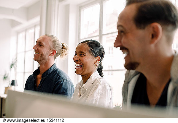 Kreative Geschäftskollegen lächeln beim Wegschauen im Büroraum