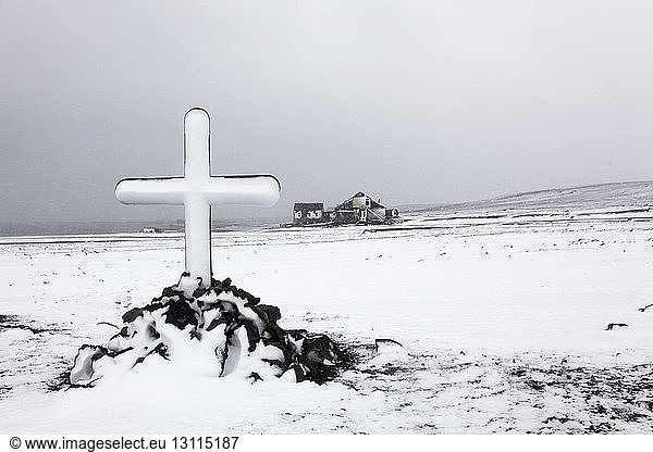 Kreuz auf schneebedecktem Feld gegen den Himmel