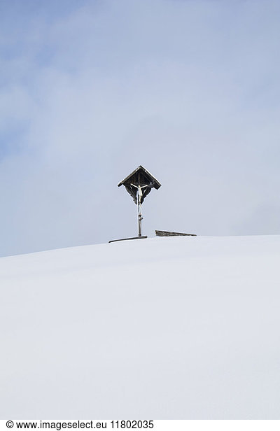 Kruzifix auf schneebedecktem Berg gegen Himmel mit Wolke
