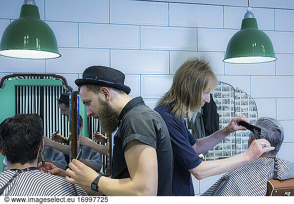 Kunden erhalten einen Haarschnitt von männlichen Friseuren in einem Friseursalon