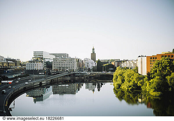 Kungsholmen Town Hall amidst modern buildings reflected in sea against clear sky