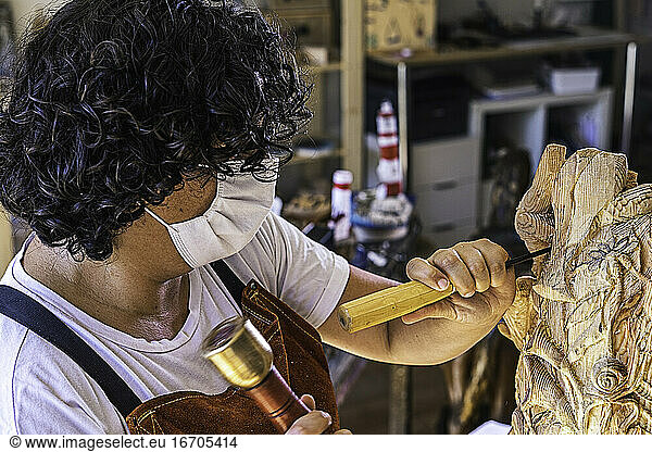 Kunsthandwerkerin mit Maske schnitzt Holzfigur