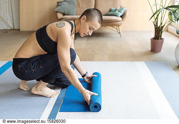 Kurzhaarige tätowierte Frau rollt Yoga-Matte in einem Dachboden aus