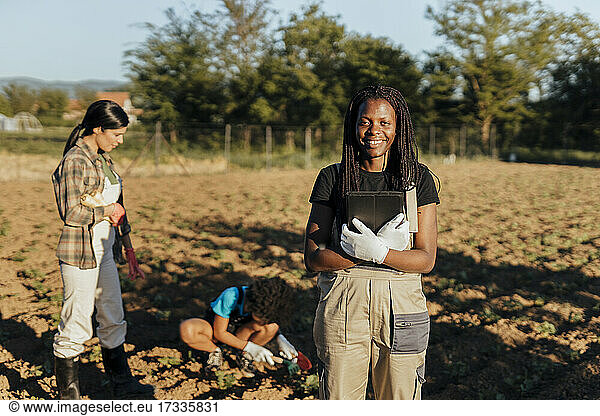 Lächelnde Bäuerin mit digitalem Tablet auf einem Bio-Bauernhof an einem sonnigen Tag