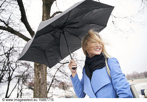 Lächelnde blonde Frau hält Regenschirm im Sturm