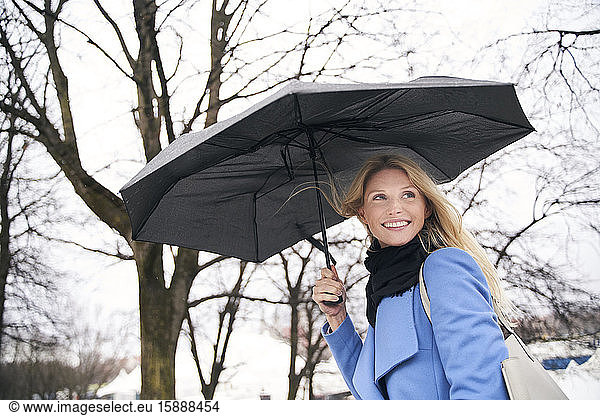 Lächelnde blonde Frau hält Regenschirm im Sturm